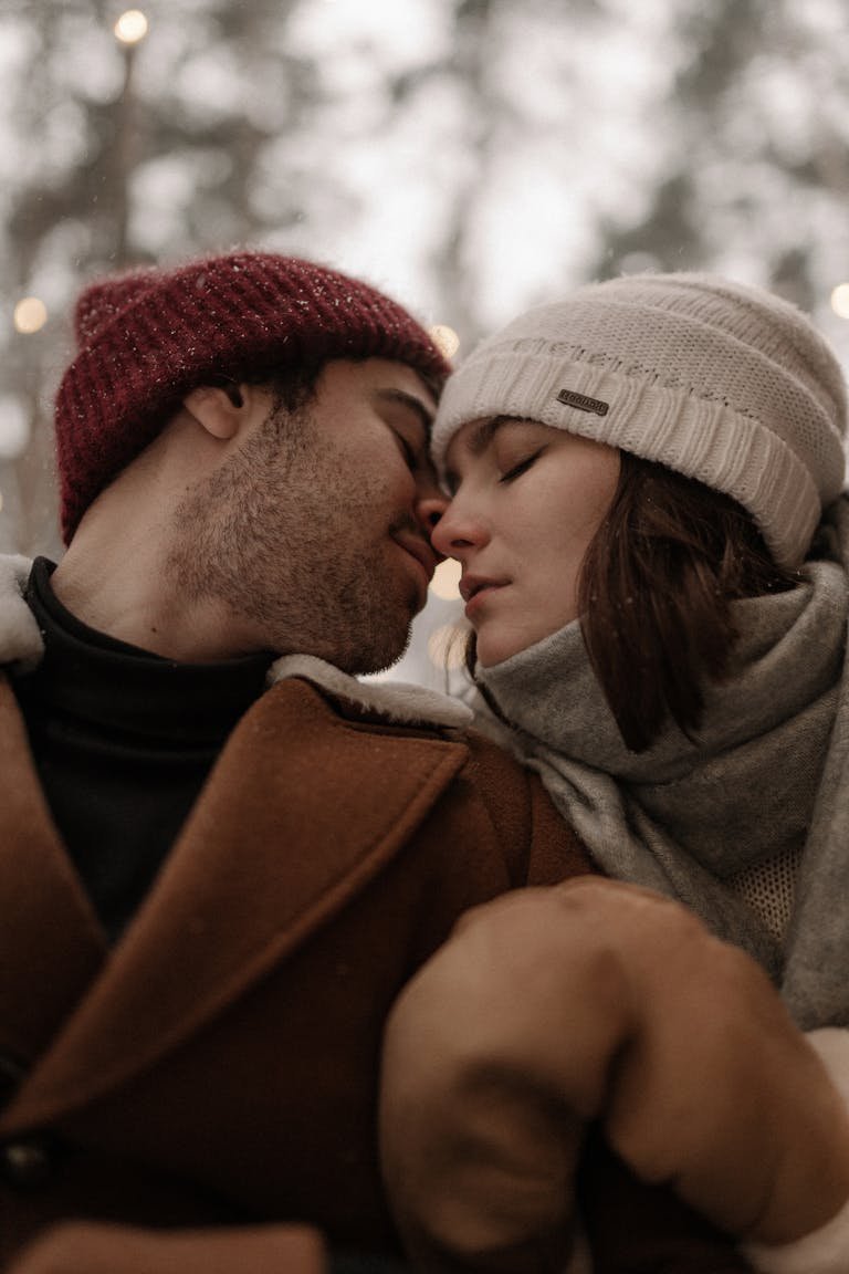 A loving couple sharing a tender moment in winter, dressed warmly in beanies and scarves.