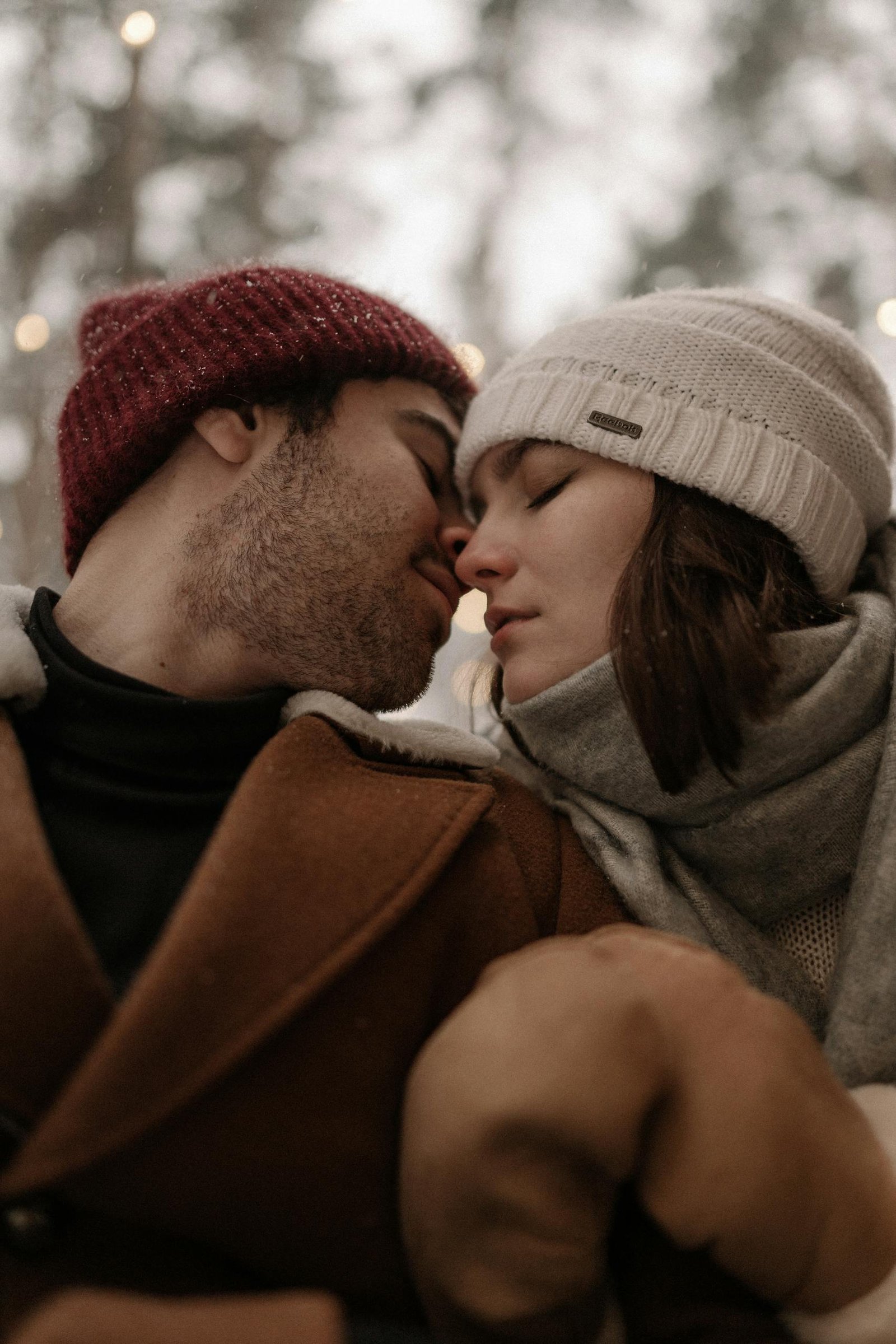 A loving couple sharing a tender moment in winter, dressed warmly in beanies and scarves.