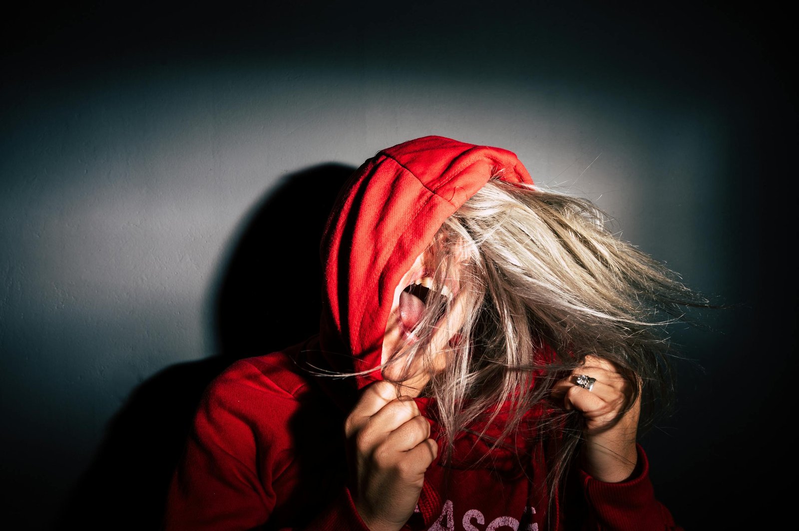 A teenager in a red hoodie screams with hair flying, conveying intense emotion.