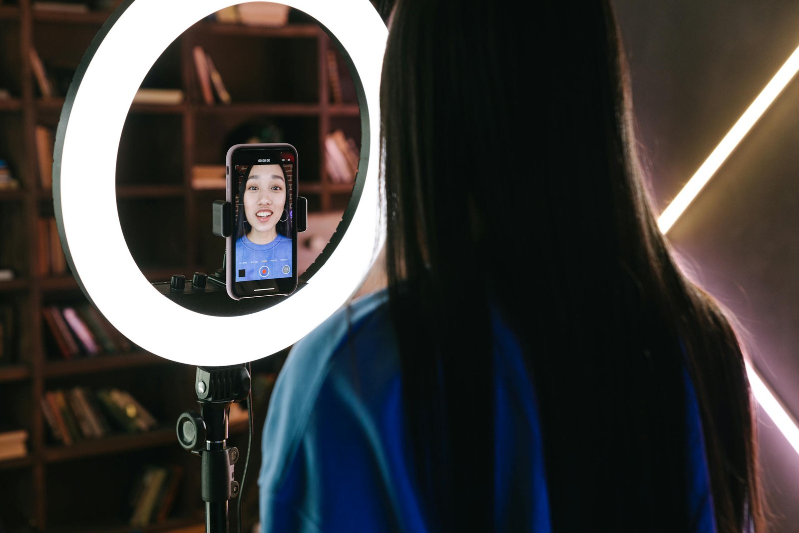 A woman records a video using a smartphone and ring light, perfect for content creators.